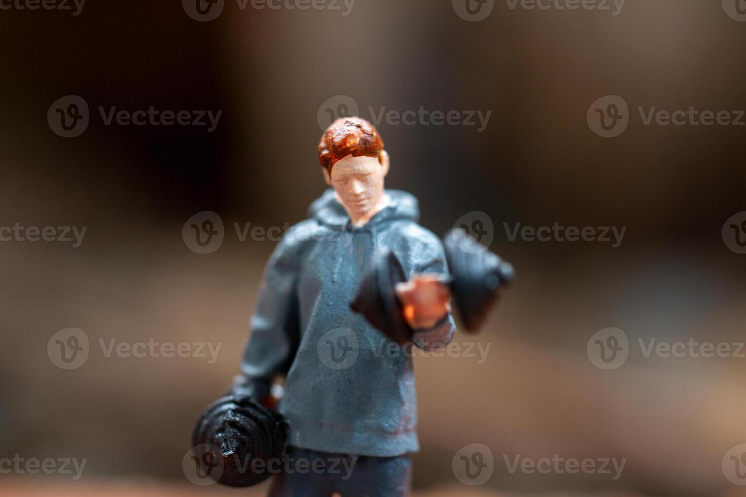 Miniature people, A man lifting dumbbells is set against a textured background photo