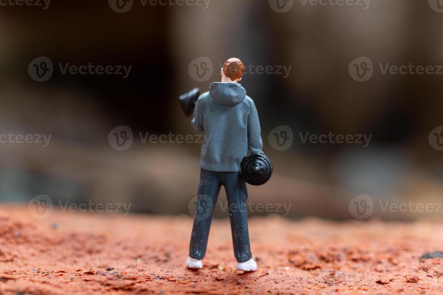 Miniature people, A man lifting dumbbells is set against a textured background photo