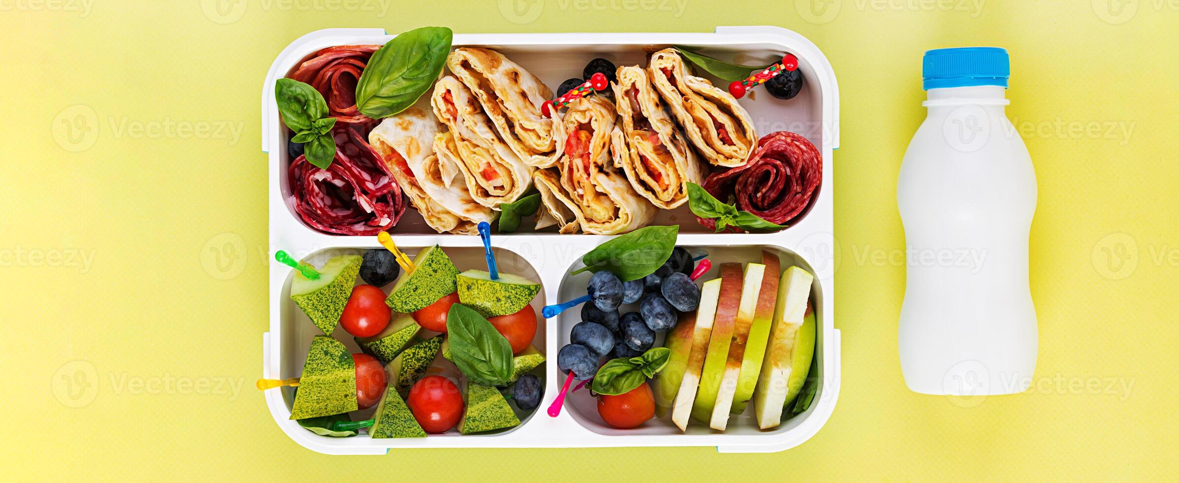 Kids lunch box with tortilla roll, sausage, cherry tomatoes and blueberries. Back to school breakfast background. Copy space. Top view, flat lay photo