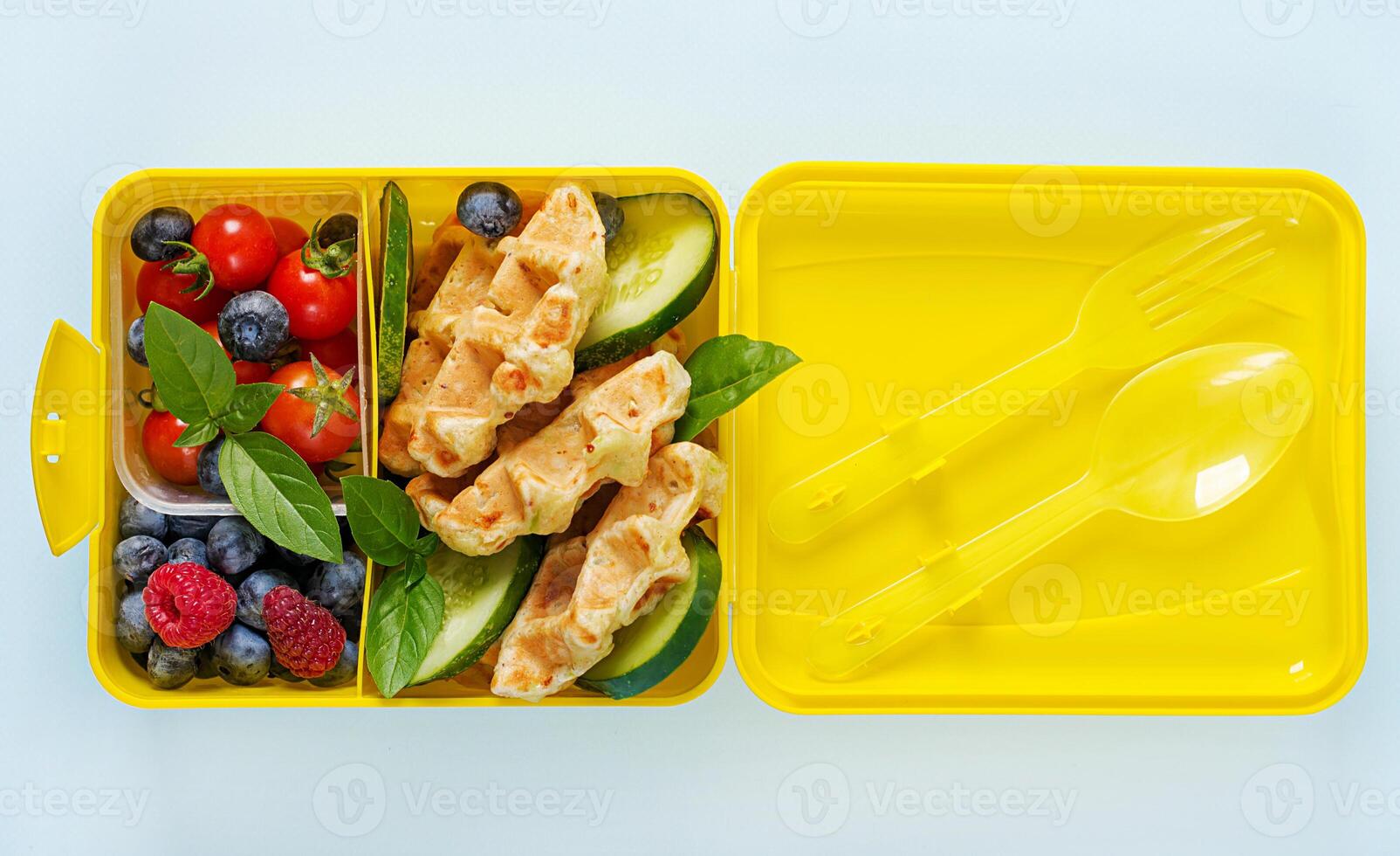 Kids lunch box with zucchini waffles, cucumber, cherry tomatoes and blueberries. Back to school breakfast background. Copy space. Top view, flat lay photo
