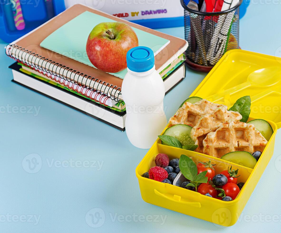 Kids lunch box with zucchini waffles, cucumber, cherry tomatoes and blueberries. Back to school breakfast background. Copy space. Top view, flat lay photo