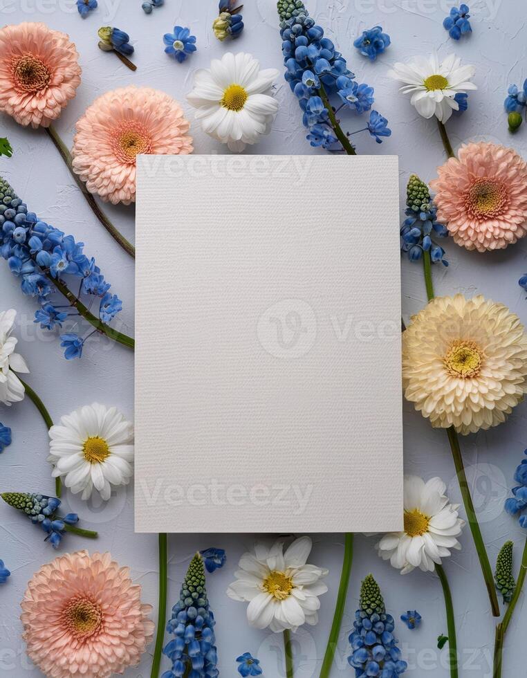 A blank card surrounded by a floral arrangement of blue pink and white blossoms photo