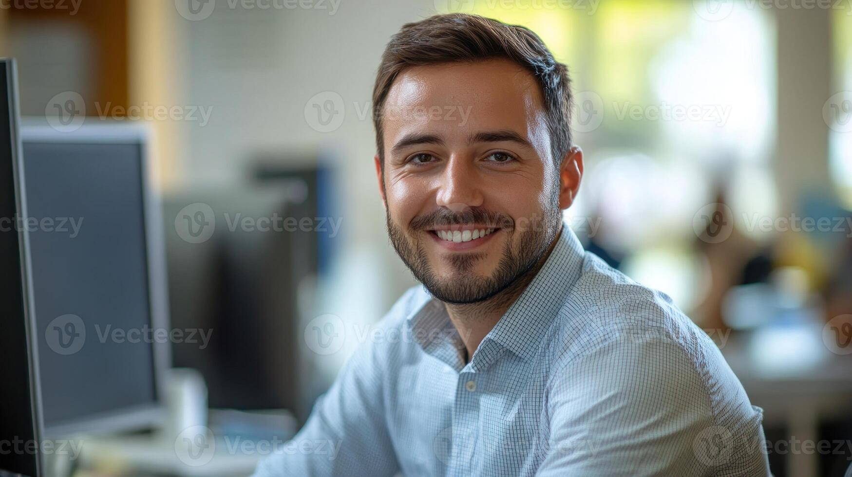 A smiling young man sits at his desk in a bright modern office space photo
