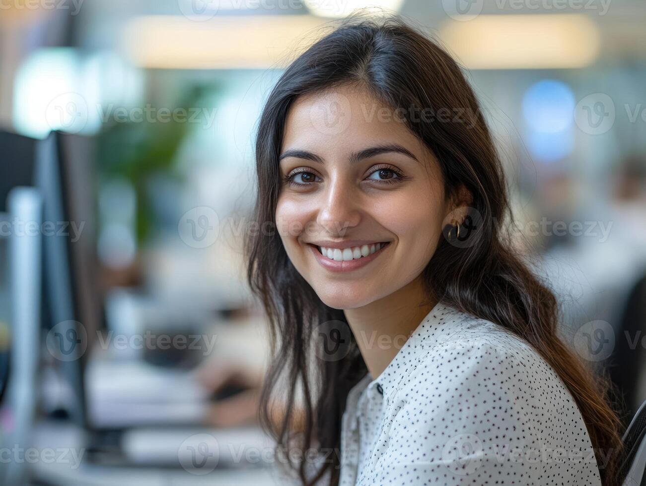 A young woman enjoys her workday, smiling brightly at her desk in a busy office photo