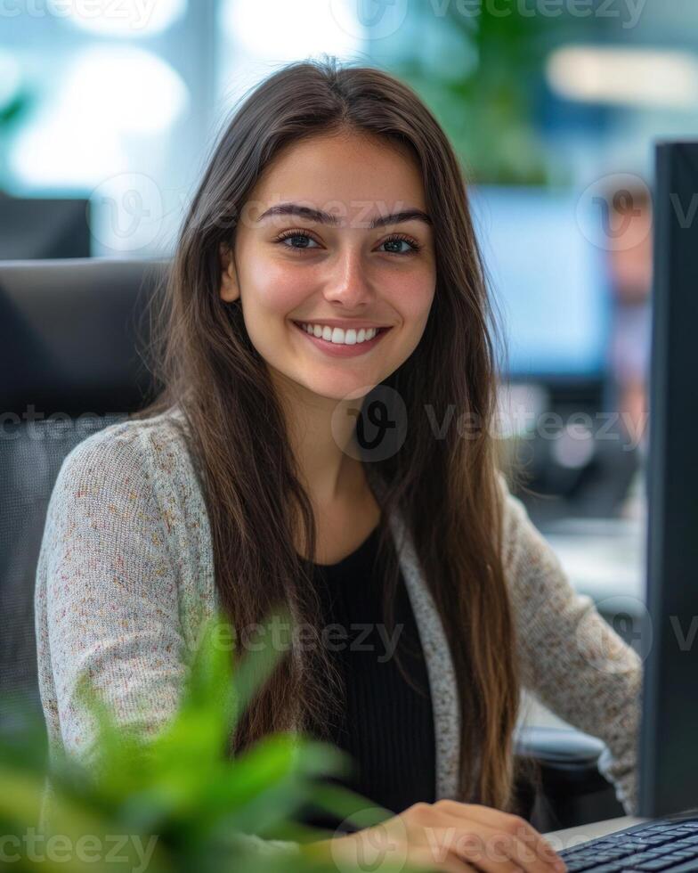A young woman smiles warmly while working at her desk in a bright office space photo