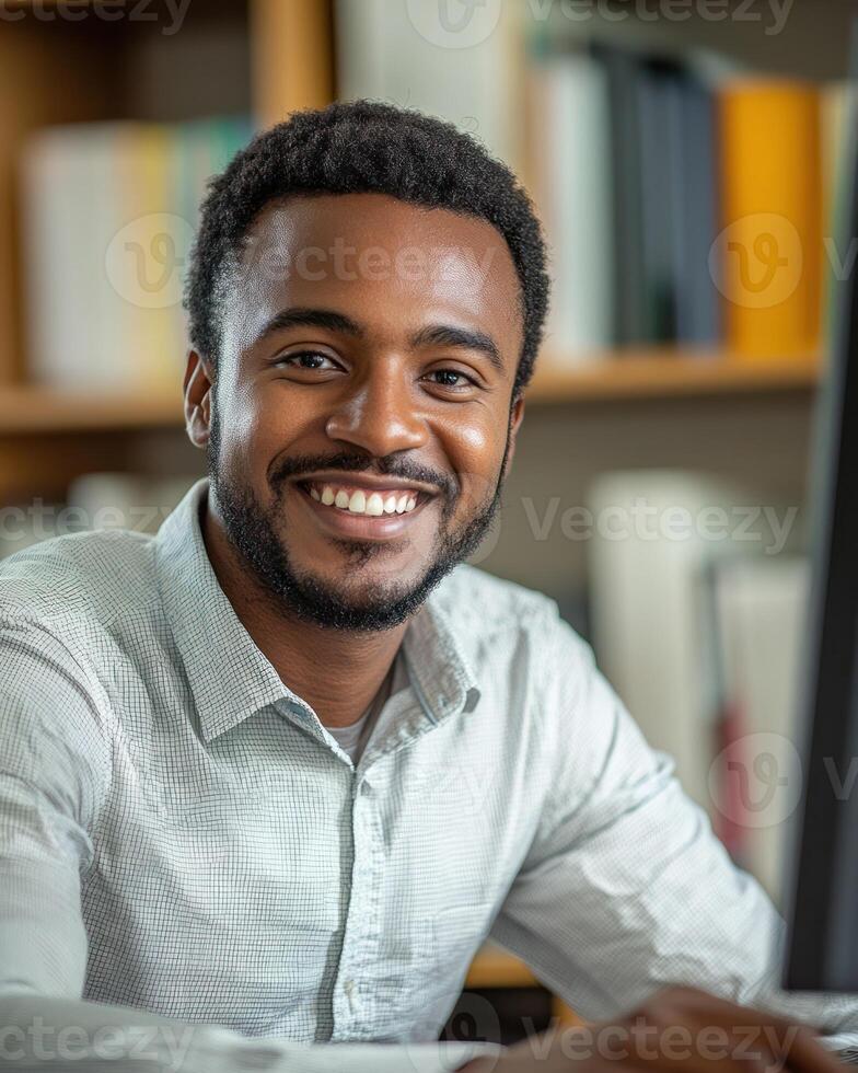 A young man smiles confidently while using a computer in a bright office space photo