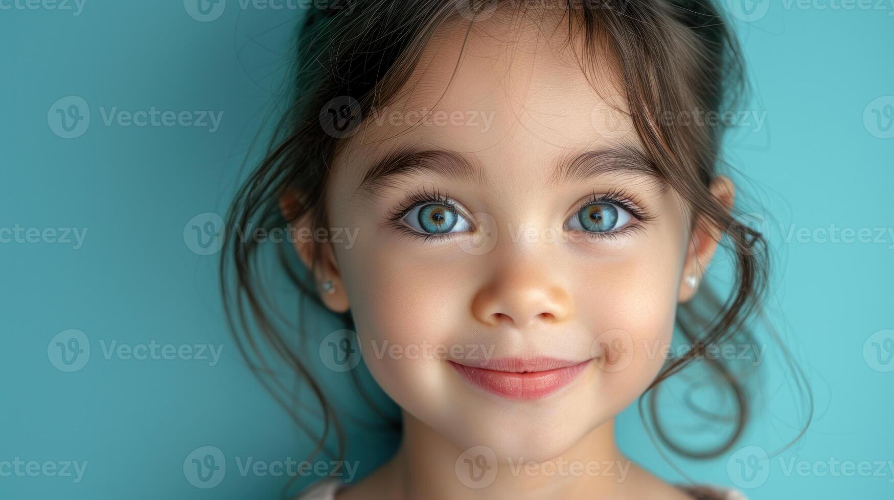 A girl with blue eyes smiles warmly while posing against a teal backdrop photo