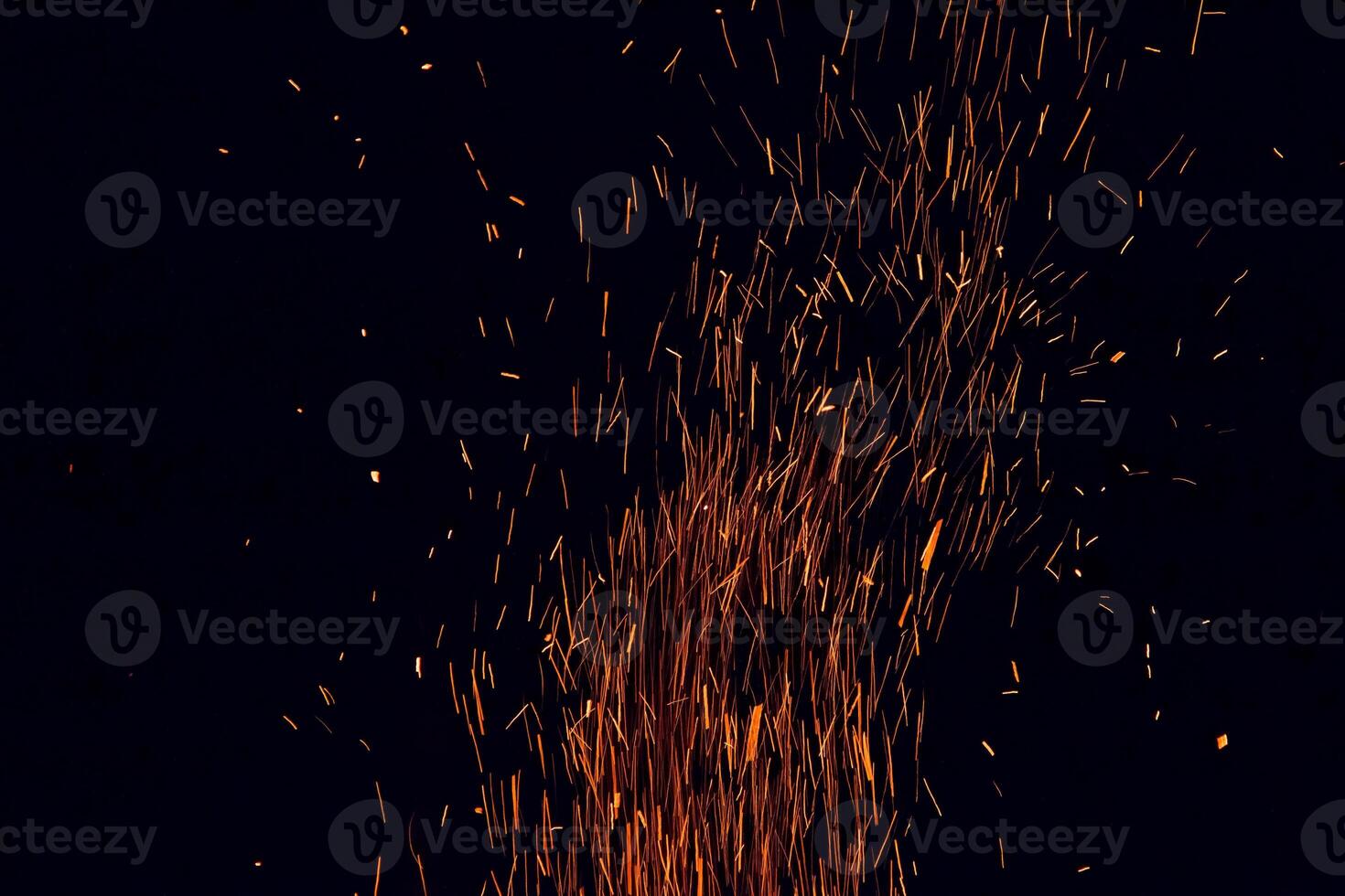 Bright burning Red and Orange Contrasting Sparks of Huge Crackling Bonfire whirl Upward against the black background of the night. Warming Campfire Lights in the Dark. A whirlwind of fire grains photo