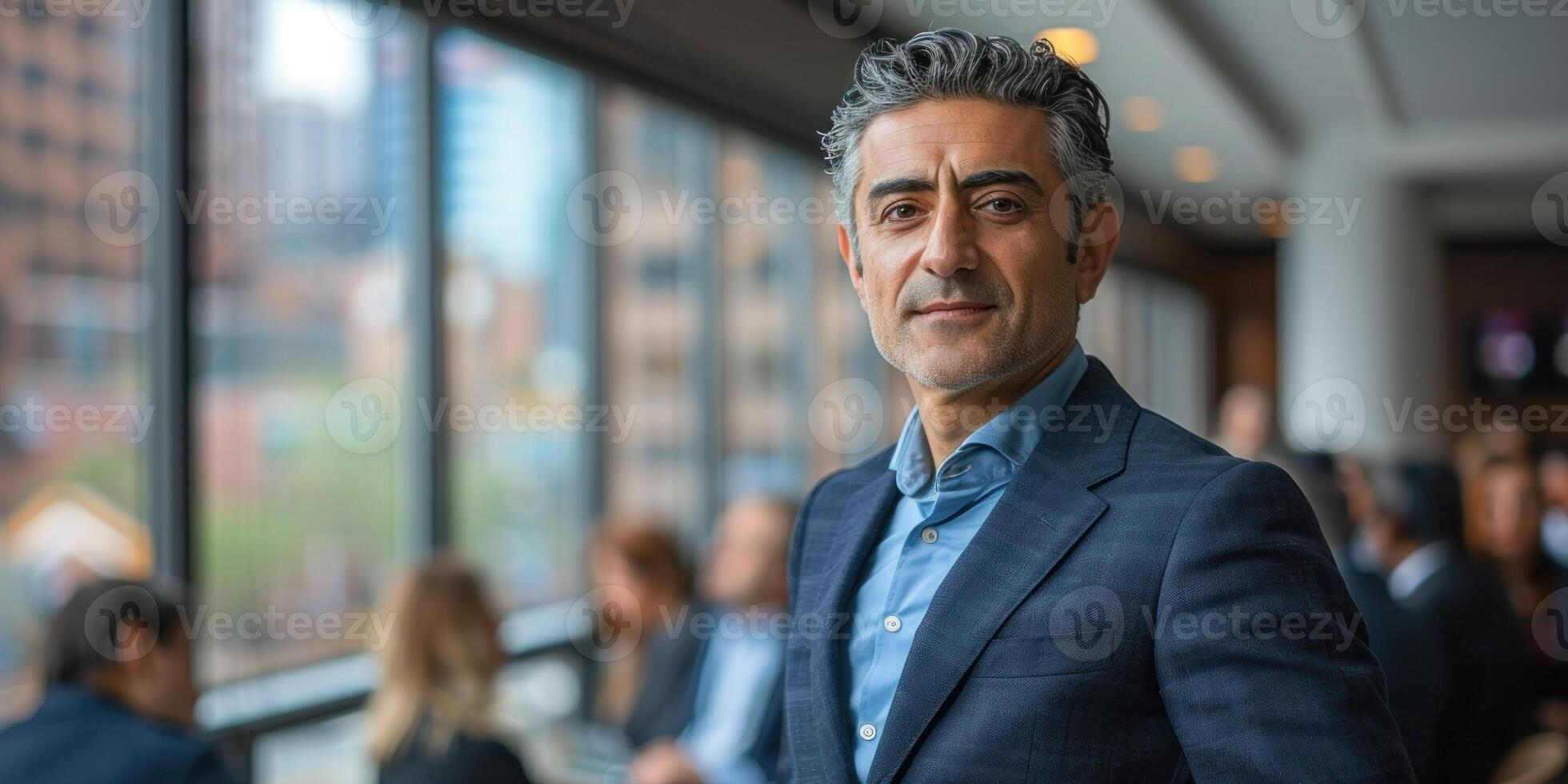 A confident man in formal attire stands among business professionals in an office setting photo