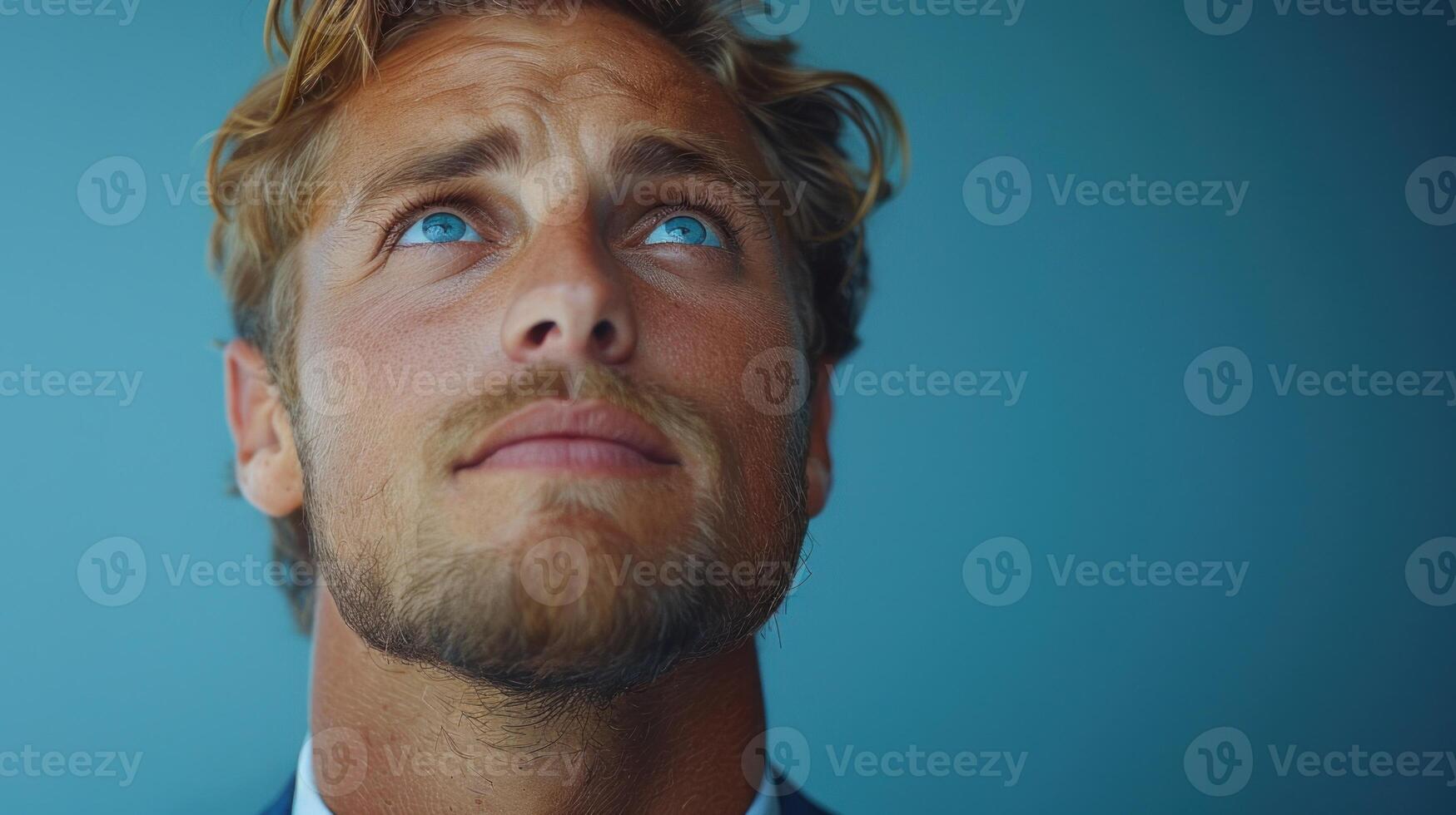 A young man gazes upward, reflecting with a thoughtful expression in a blue setting photo