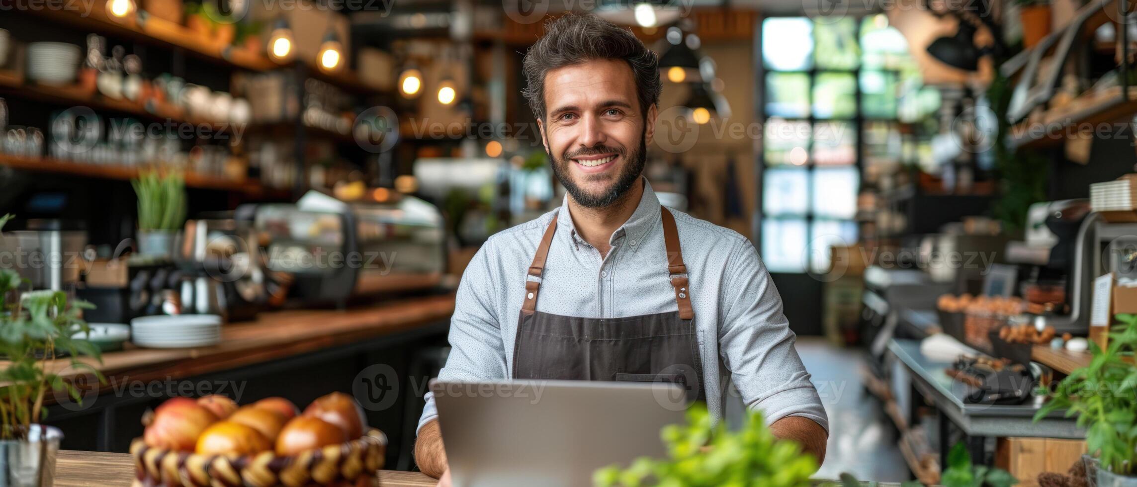 A man in a cafe smiles at the camera while using a laptop photo