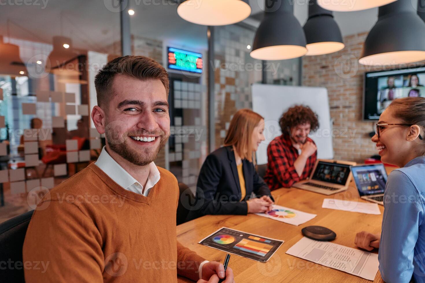 In the vibrant ambiance of a modern startup office, a diverse team of business professionals engage in discussions on various projects and develop new business strategies, epitomizing creativity and photo