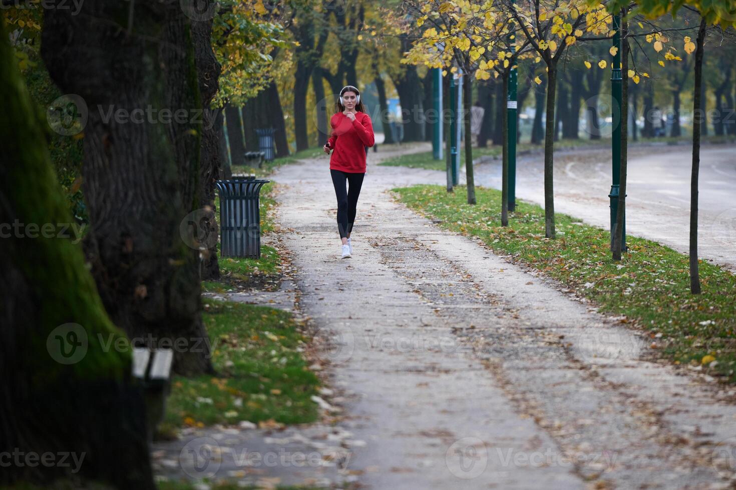 Young beautiful woman running in autumn park and listening to music with headphones on smartphone photo