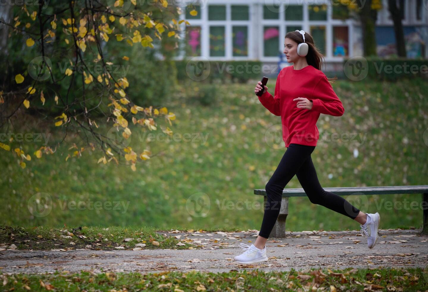 Young beautiful woman running in autumn park and listening to music with headphones on smartphone photo