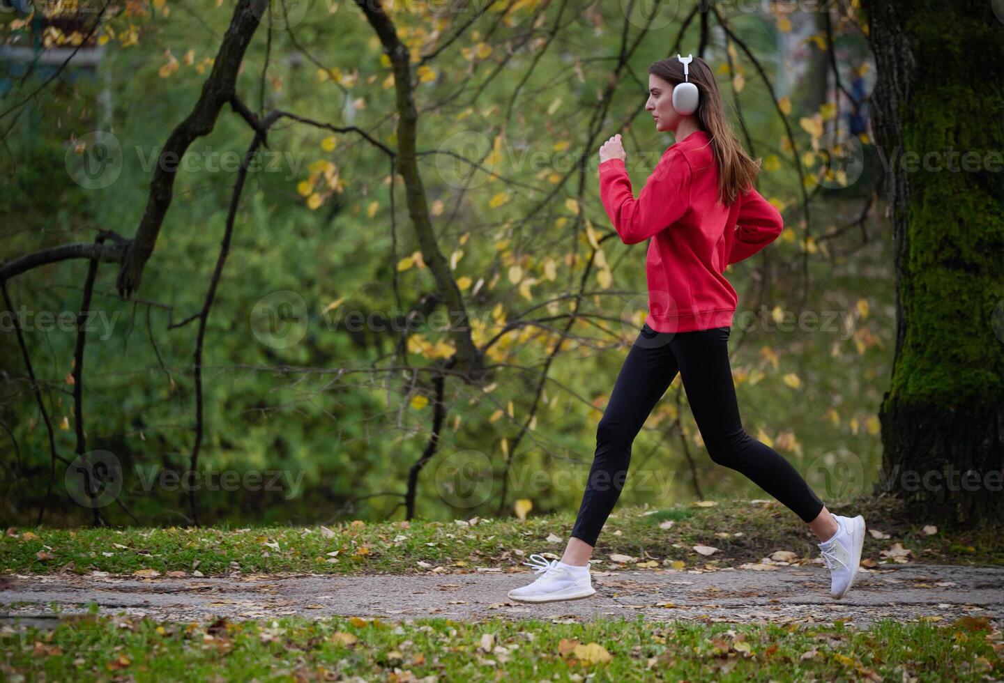 Young beautiful woman running in autumn park and listening to music with headphones on smartphone photo
