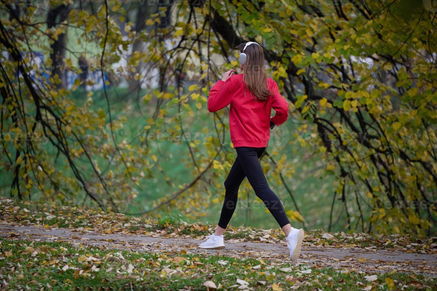 Young beautiful woman running in autumn park and listening to music with headphones on smartphone photo