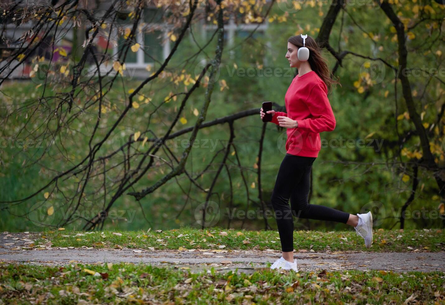 Young beautiful woman running in autumn park and listening to music with headphones on smartphone photo