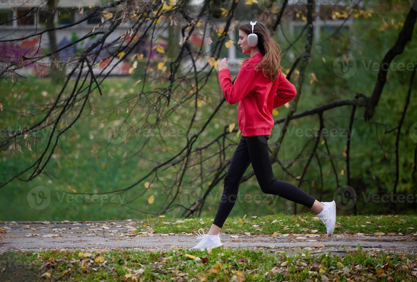Young beautiful woman running in autumn park and listening to music with headphones on smartphone photo