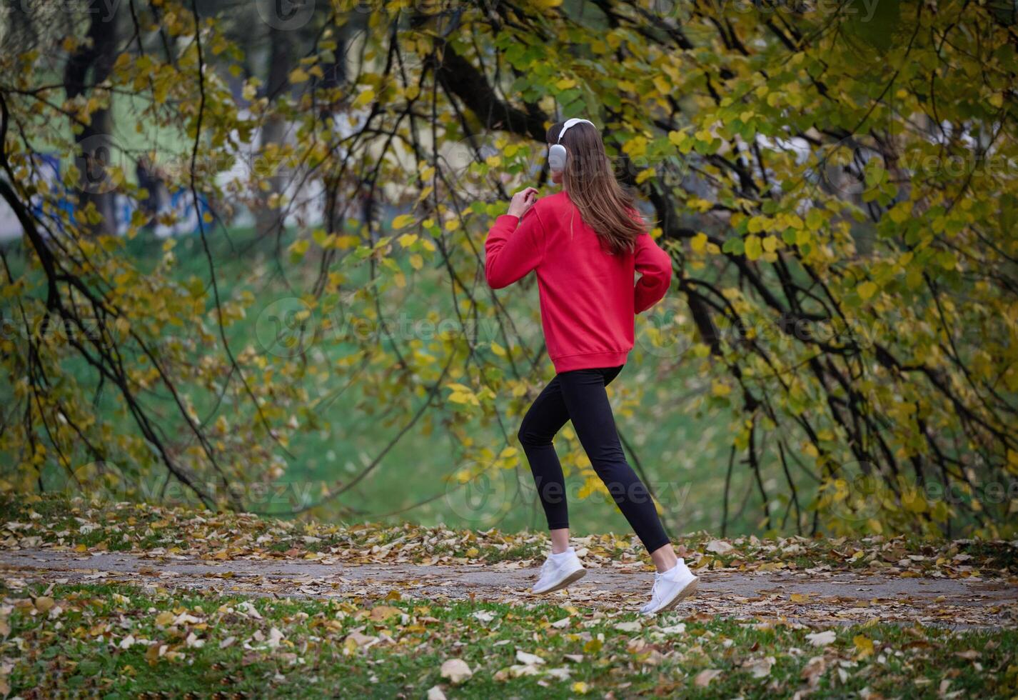 Young beautiful woman running in autumn park and listening to music with headphones on smartphone photo