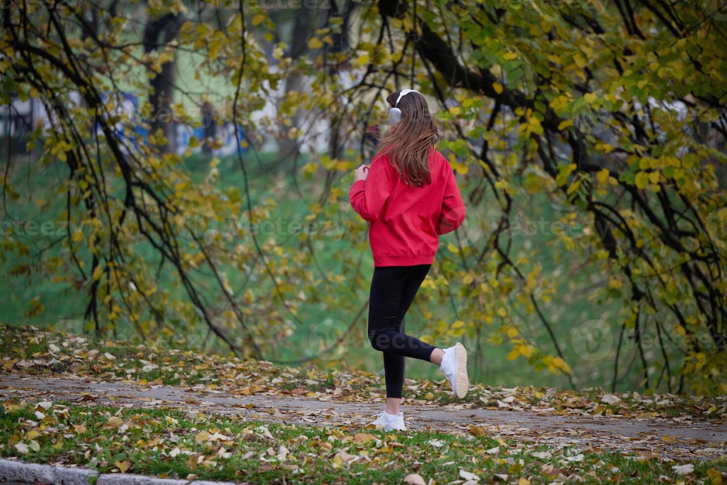 Young beautiful woman running in autumn park and listening to music with headphones on smartphone photo