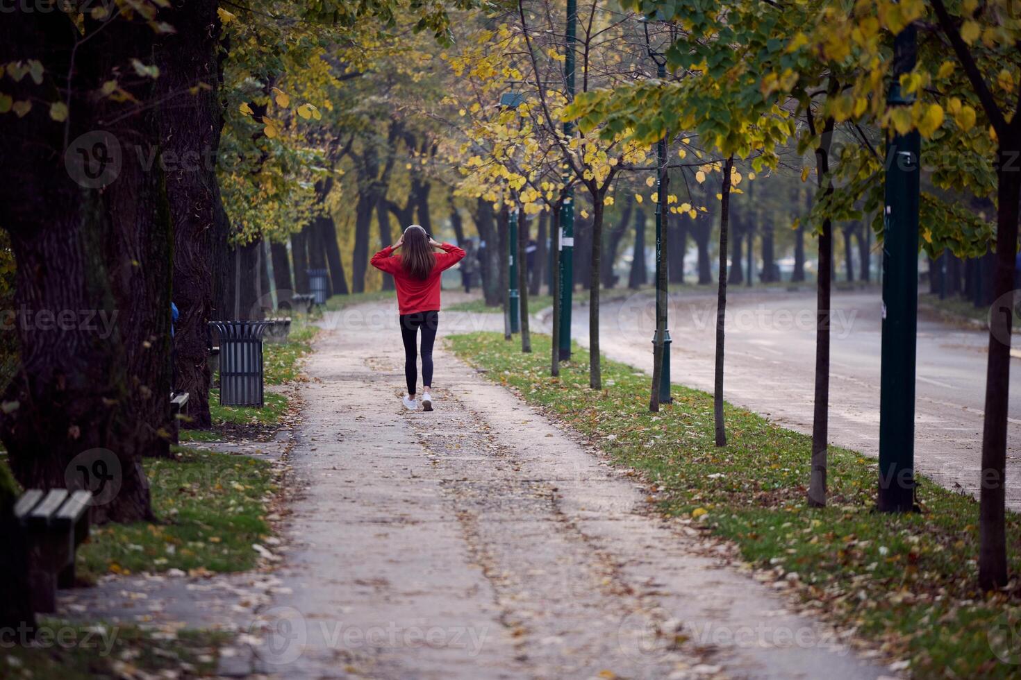 Young beautiful woman running in autumn park and listening to music with headphones on smartphone photo