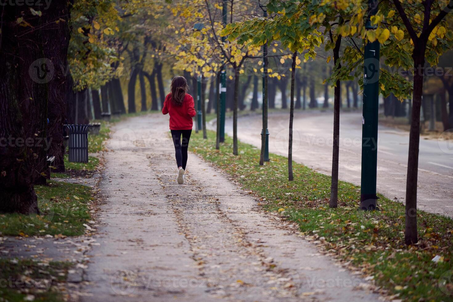 Young beautiful woman running in autumn park and listening to music with headphones on smartphone photo