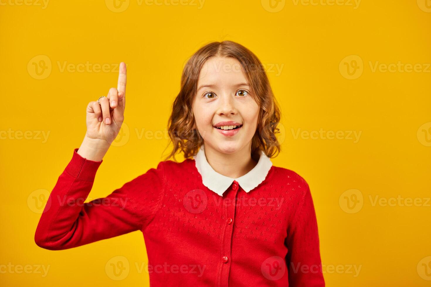 Teenage Schoolgirl in Red Cardigan Pointing Upwards Against a Yellow Background photo
