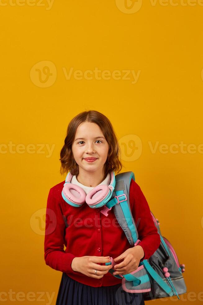 Smiling Teenage Schoolgirl With Backpack and Headphones Against Yellow Background photo