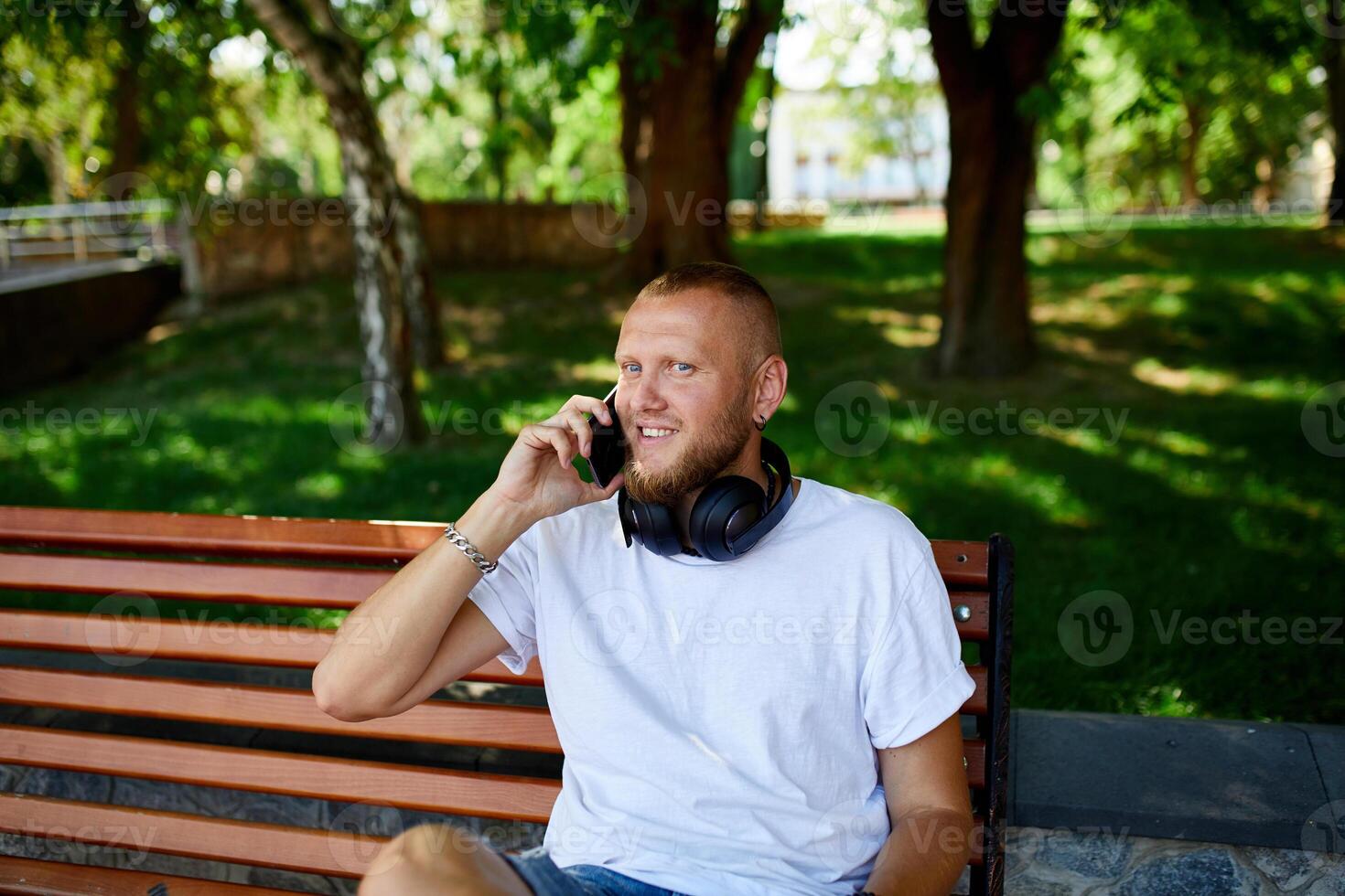 Smiling Man With Headphones Talking on Phone in Sunny Park photo