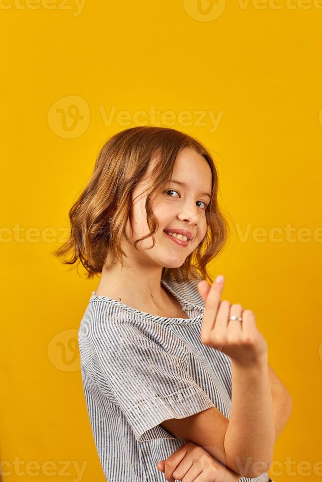 Schoolgirl Making Heart Shape With Hands Against a Vibrant Yellow Background photo