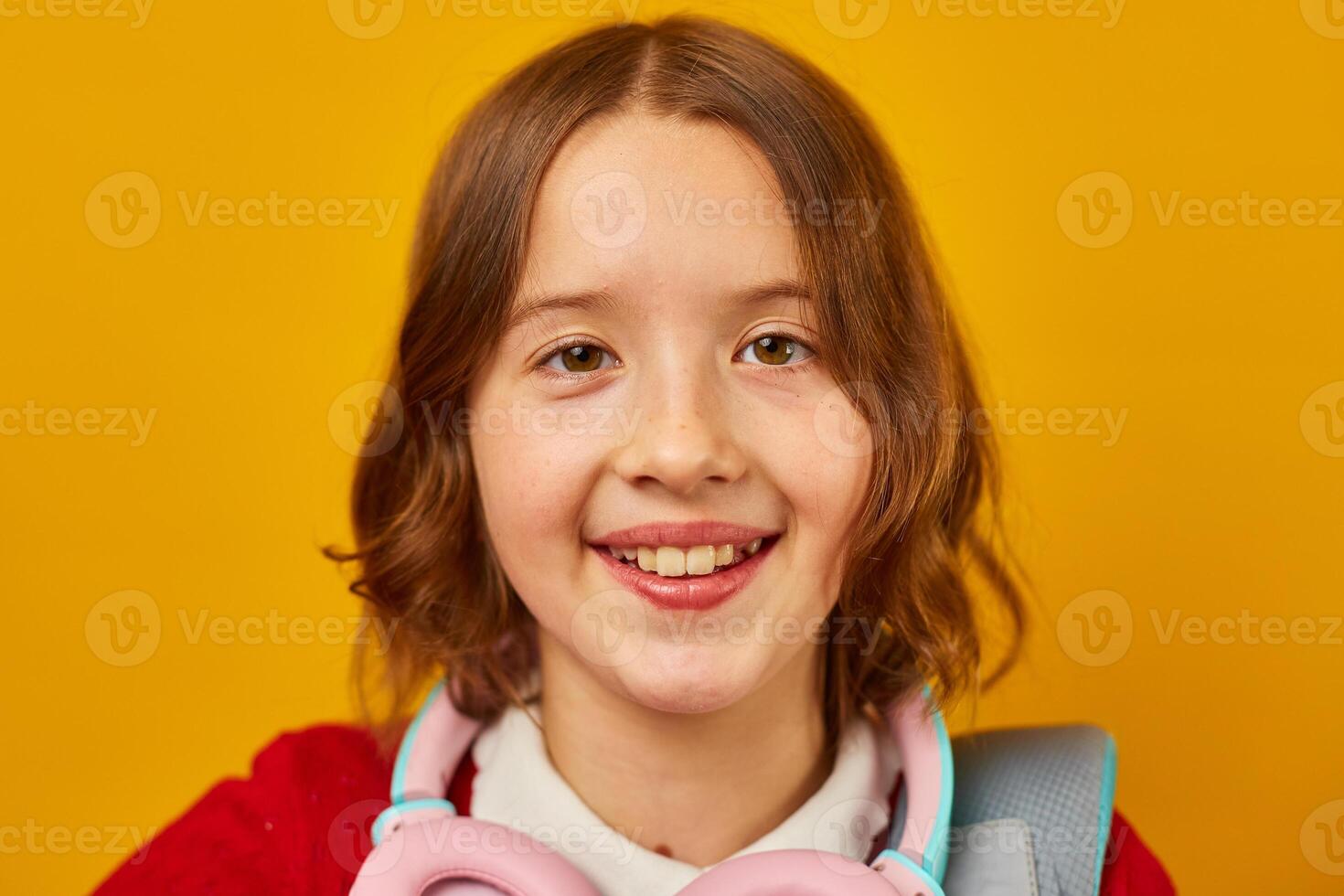 Smiling Teenage Schoolgirl With Backpack and Headphones Against Yellow Background photo