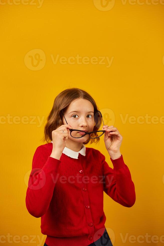 Teenage Girl in School Uniform Holding Glasses Against a Bright Yellow Background photo