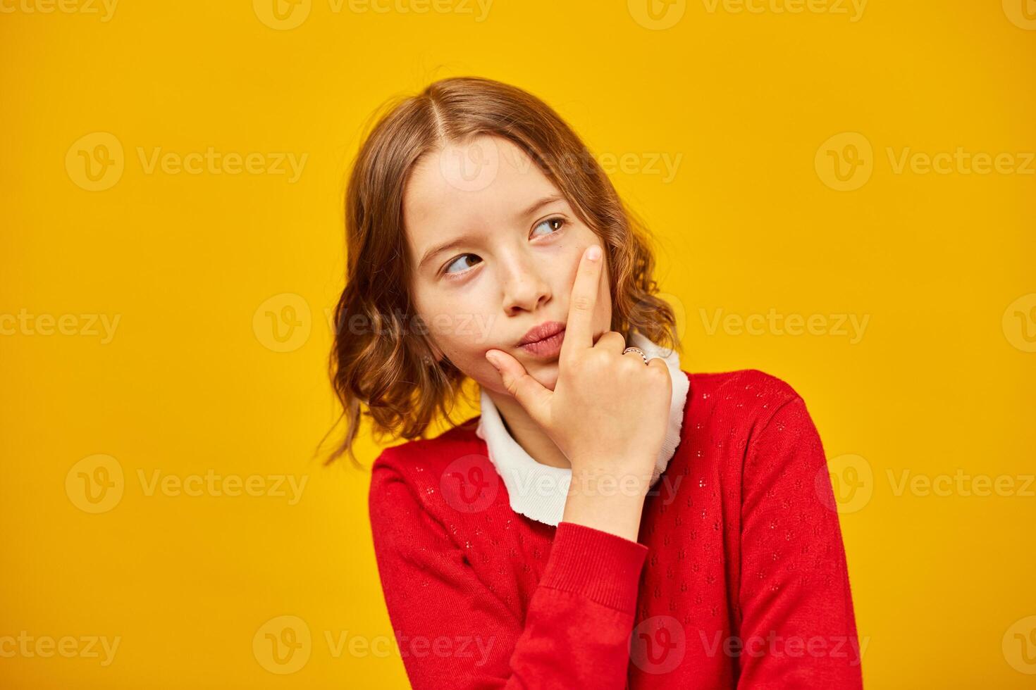 Thoughtful Teenage Schoolgirl Posing in Red Sweater Against Yellow Background photo