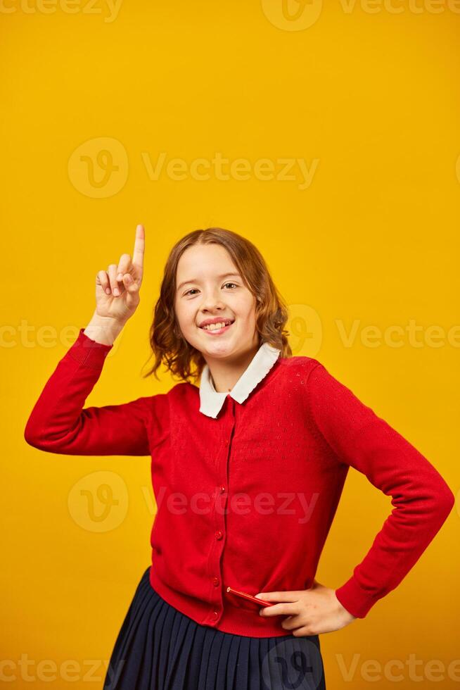 Teenage Schoolgirl in Red Cardigan Pointing Upwards Against a Yellow Background photo