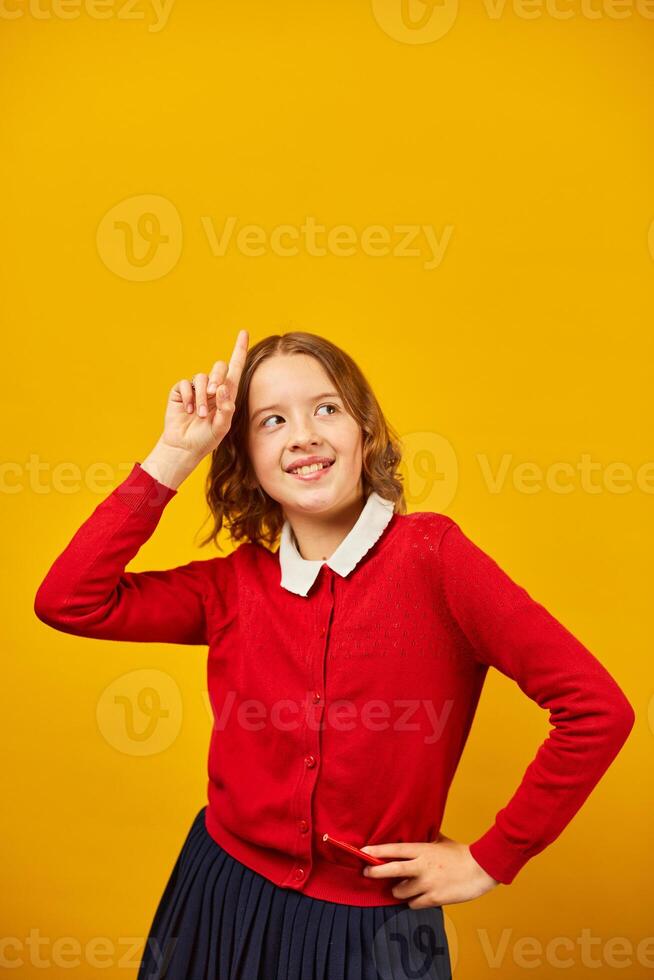 Teenage Schoolgirl in Red Cardigan Pointing Upwards Against a Yellow Background photo