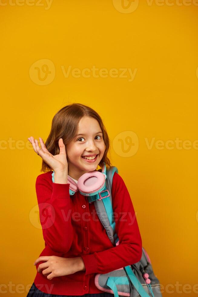 Smiling Teenage Schoolgirl With Backpack Pointing to Head Against Yellow Background photo