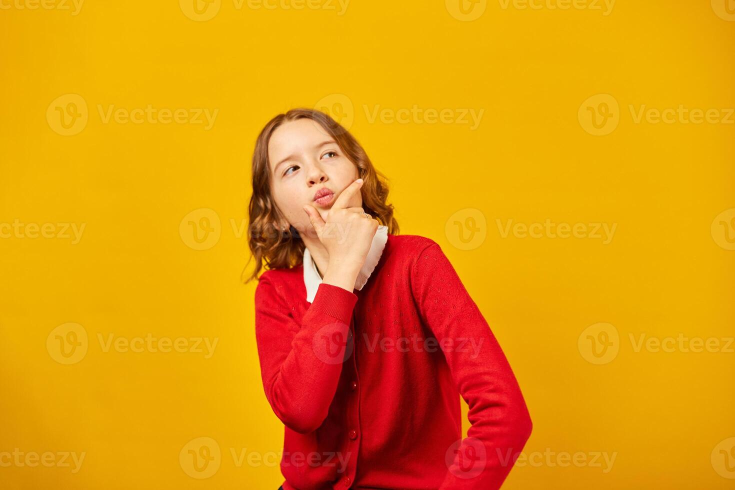 Thoughtful Teenage Schoolgirl Posing in Red Sweater Against Yellow Background photo