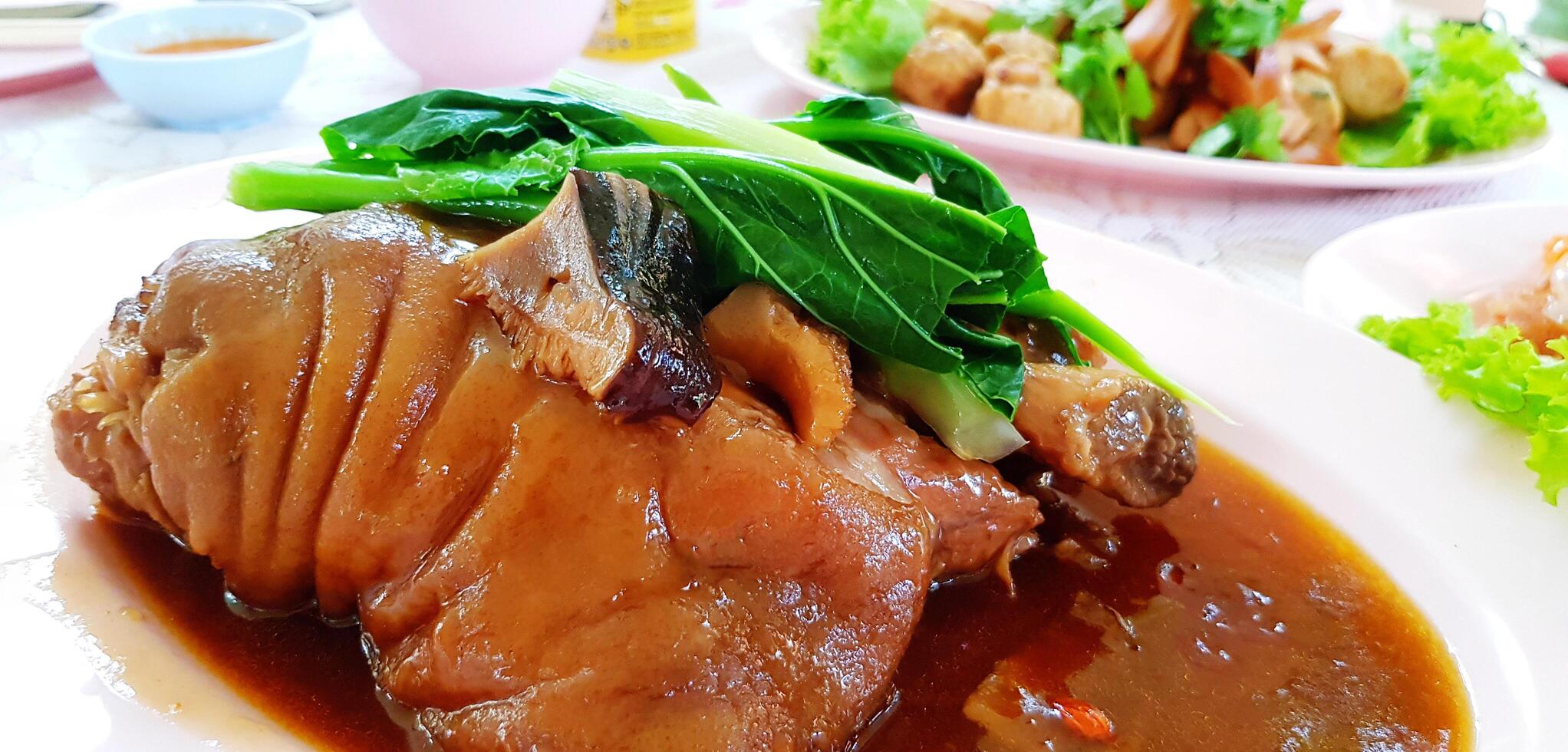 Close up Stewed pork leg with Chinese kale and mushroom on top in plate with another food background. Unhealthy food, eating and Fat concept. photo