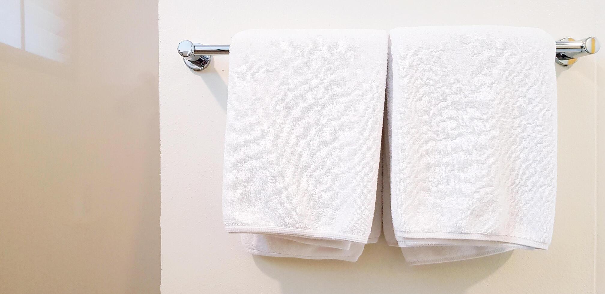 Two white clean towel and napkin hanging on stainless hanger with white wall background for customer using in bathroom with copy space. Cleaning, Shape and Surface of stone concept. photo