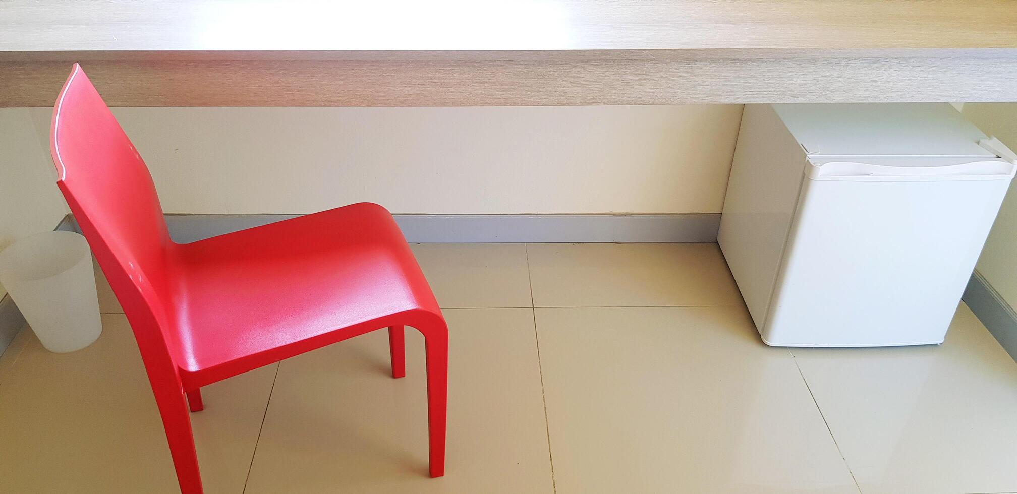 Red chair with white refrigerator, white garbage putting on tile floor and wooden shelf in private room. Interior design and Modern furniture concept photo