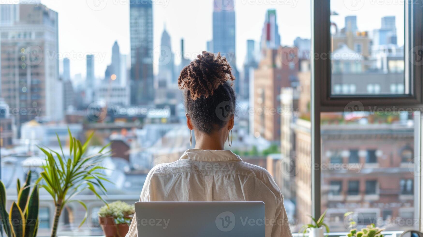 A woman sits at a desk working on her laptop, overlooking a bustling cityscape from a high-rise window with indoor plants. photo