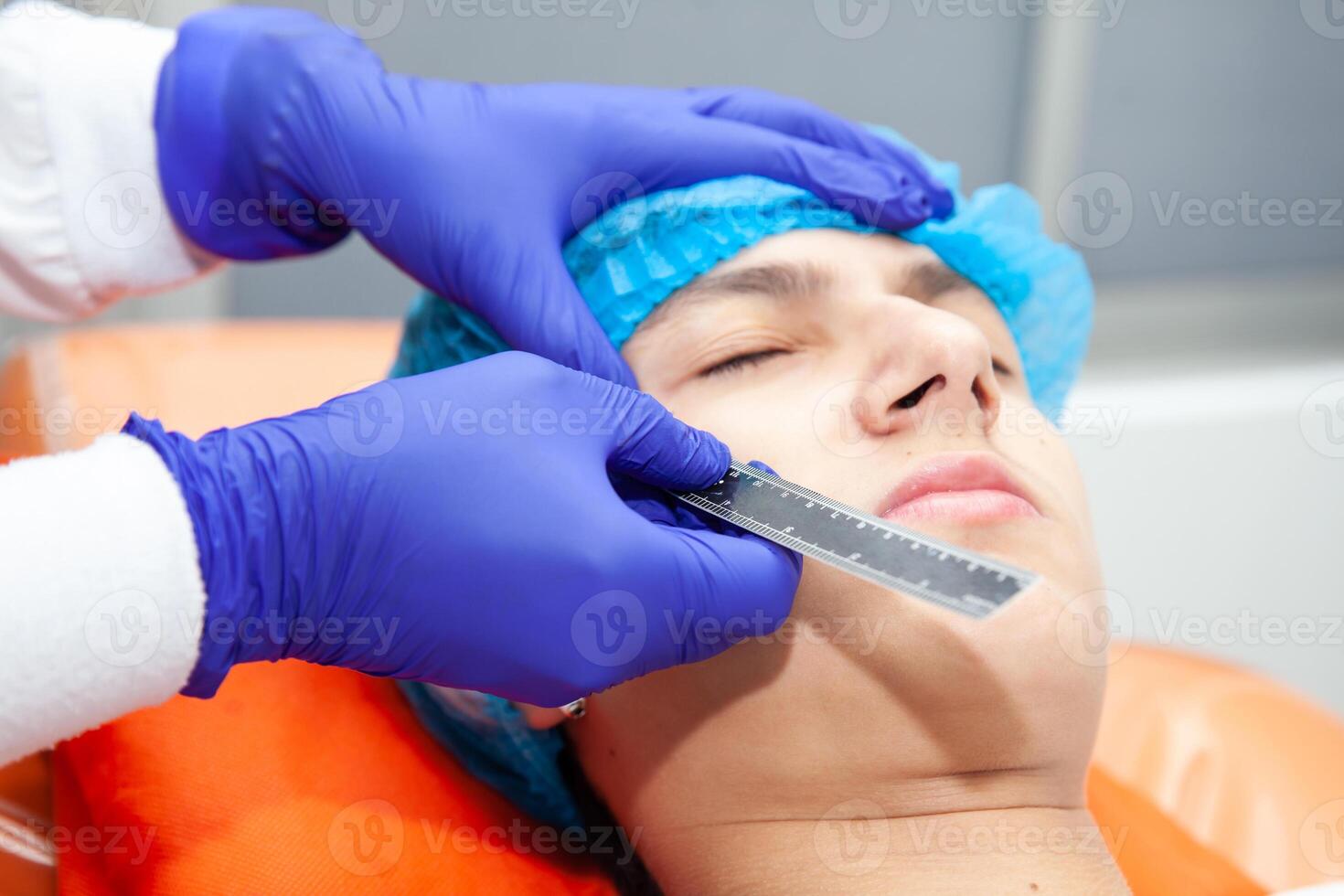 Skin lesion removal procedure. Dermatologist carrying out a removal of benign skin lesion on the face of a young male patient. photo
