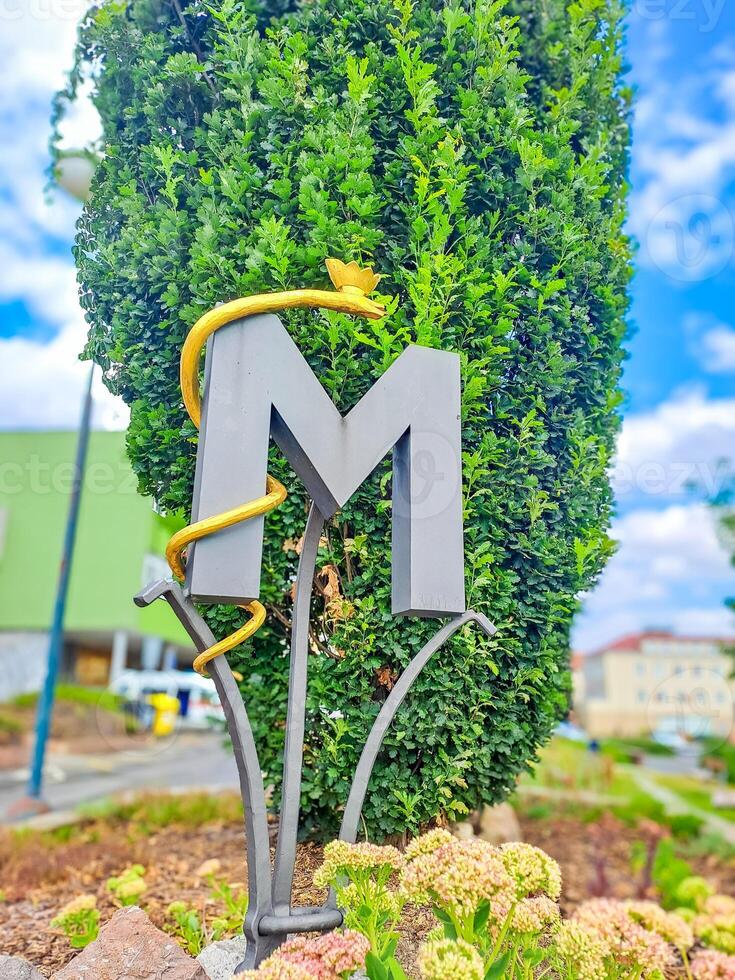 Ornate decoration of fence with artistic monogram, letter M with a snake. Czech photo