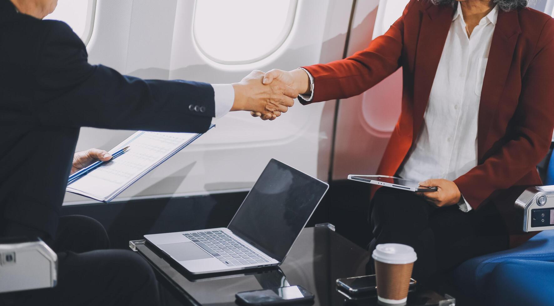 business people at meeting in private plane, Asian businessman in suit is talking to woman in jet and pointing at blank laptop screen, colleagues are discussing deal and flying in plane photo