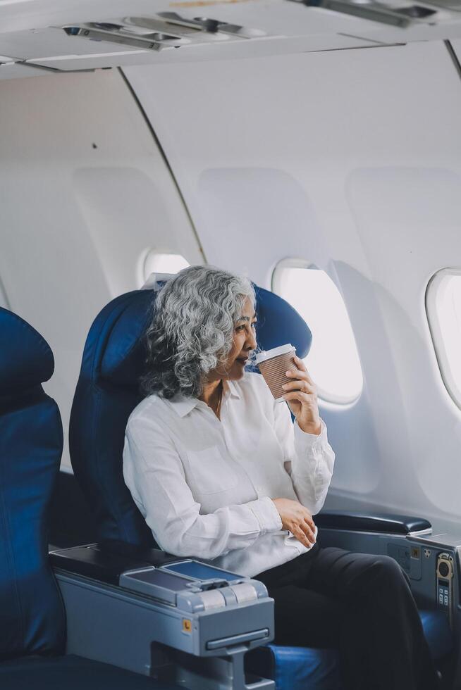 An attractive, elegant Asian businesswoman is sipping coffee while looking at the view outside the plane window, traveling on a business trip. businesspeople, transportation, luxurious lifestyle photo