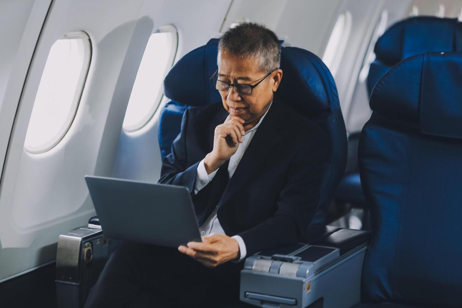 Attractive Asian male passenger of airplane sitting in comfortable seat while working laptop and tablet with mock up area using wireless connection. Travel in style, work with grace. photo