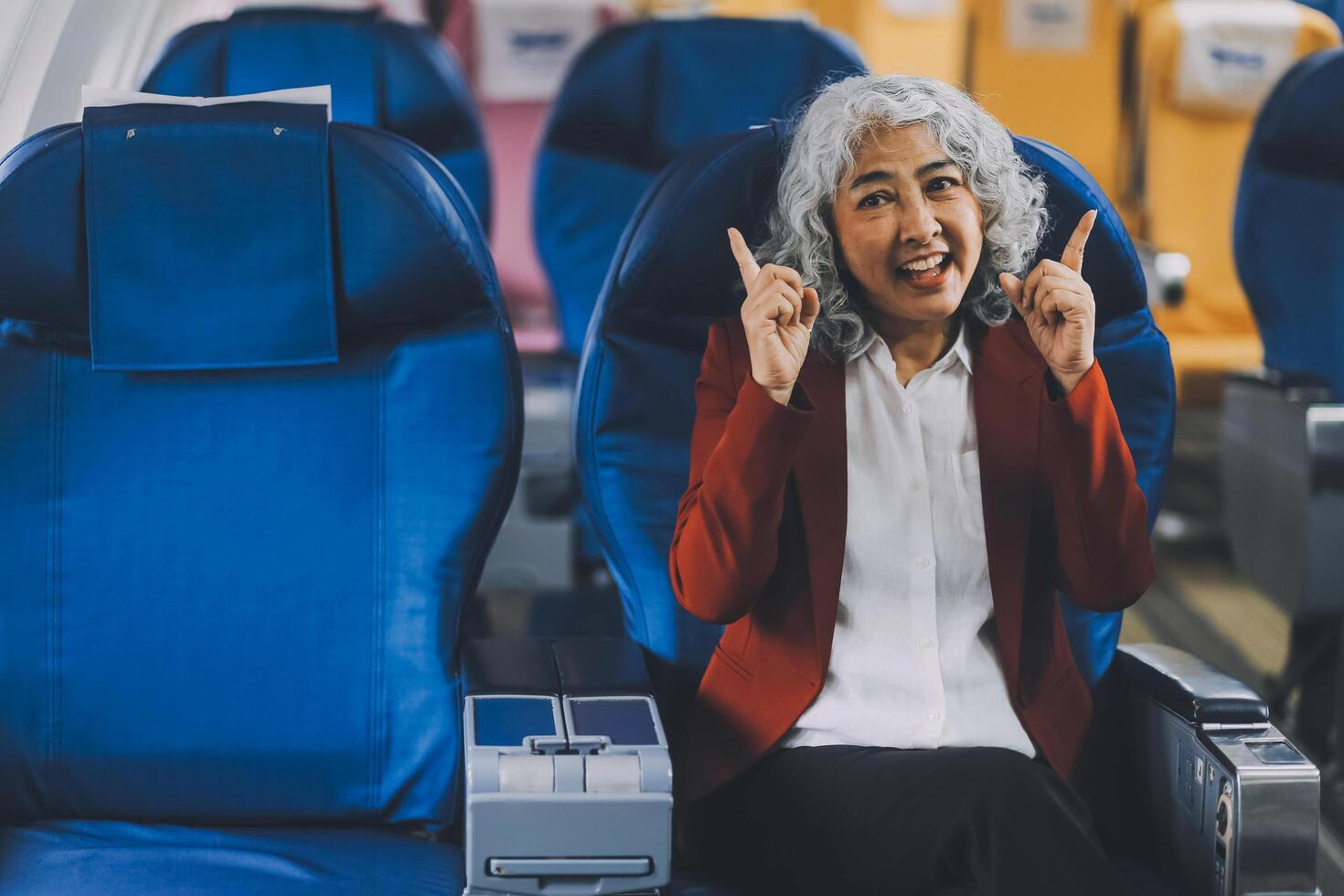 Portrait of a successful Asian businesswoman or entrepreneur in a formal suit on an airplane sitting in business class using a phone, computer laptop. Travel in style, work with grace. photo