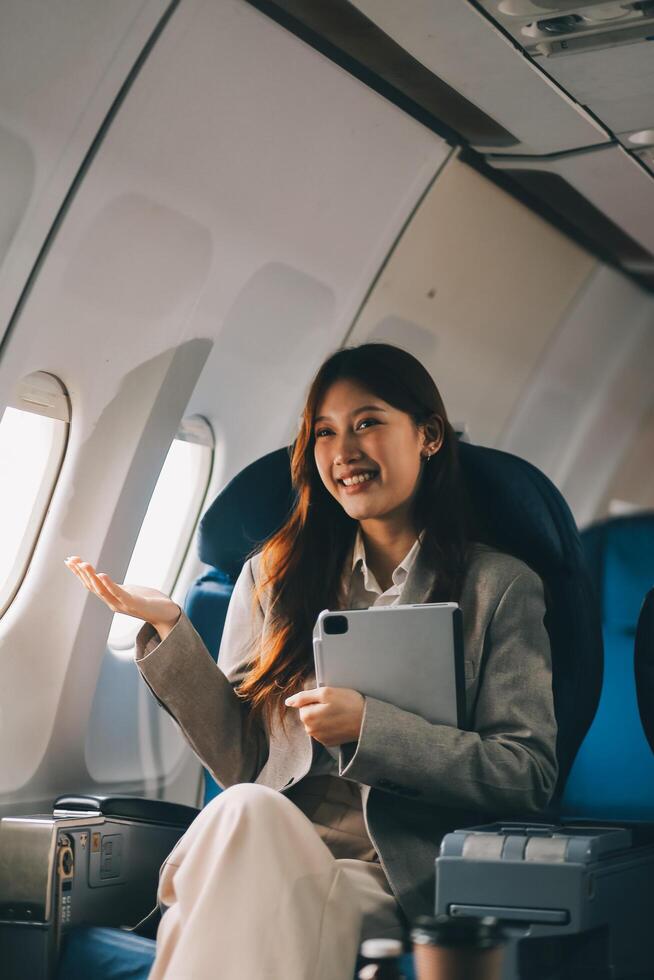 Joyful asian woman sits in the airplane and using tablet while go to travel photo