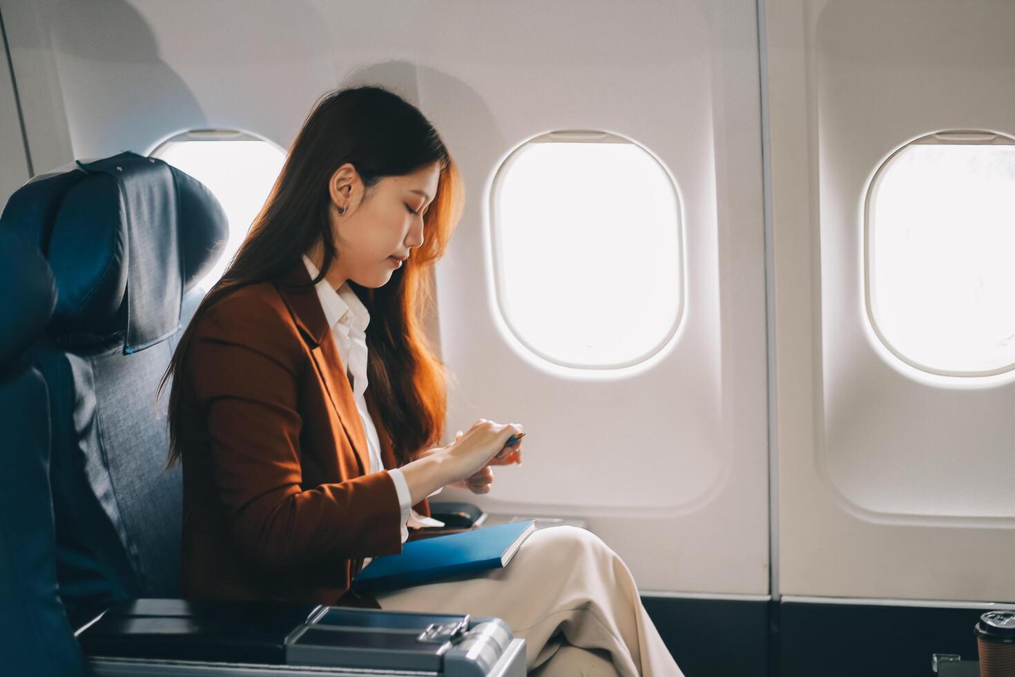 Asian woman looking at phone while sitting on airplane Technology female travelers using mobile smartphones, online apps, and the internet while sitting in airplane seats during travel. photo