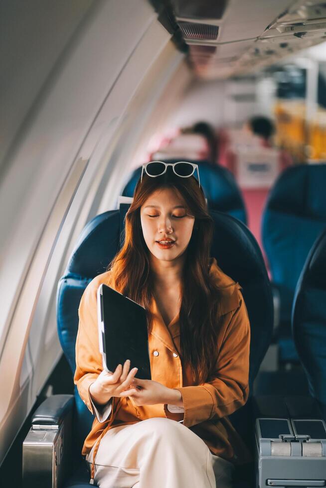 Joyful asian woman sits in the airplane and using tablet while go to travel photo